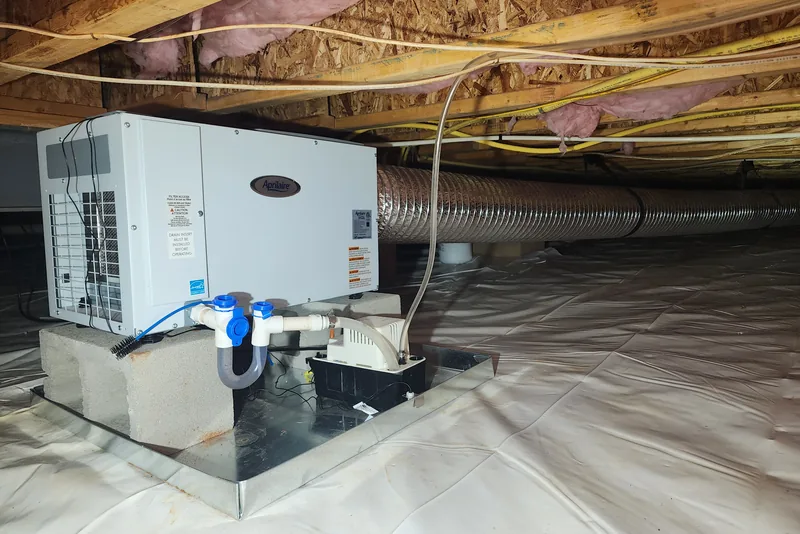 Aprilaire dehumidifier installed on vapor barrier in an encapsulated crawl space in NC, with condensate pump and drain lines plumbed and ready