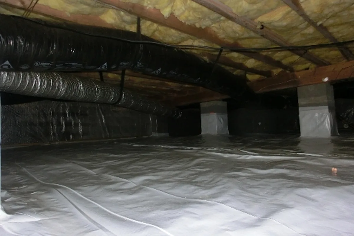 Crawl space vapor barrier covering the dirt floor with flexible HVAC duct and fiberglass insulation visible above the joists in a Wake County NC home